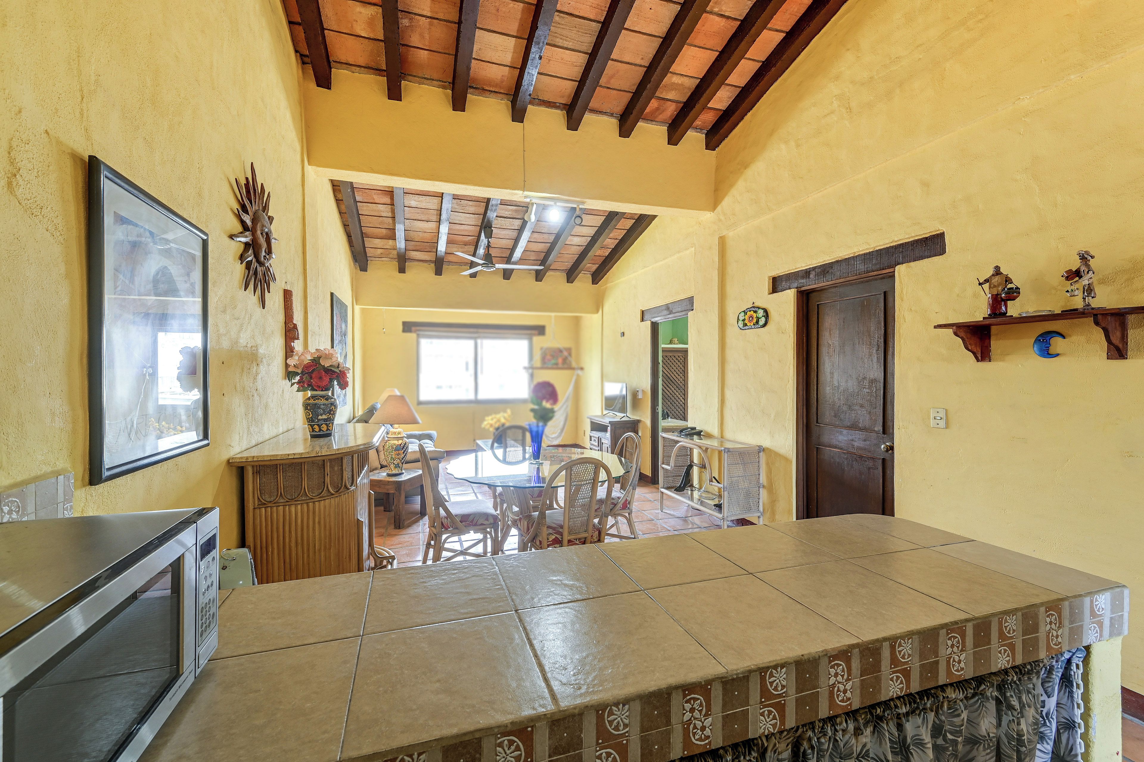 Un vaste espace de vie doté d’un plancher carrelé, d’un ventilateur de plafond et d’un coin repas avec des chaises et une table.