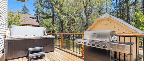 A deck with a hot tub, a grill, and a wooden structure.
