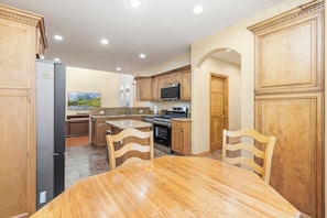 A kitchen with wooden cabinets, a refrigerator, a microwave, an oven, and a dining table with chairs. - Hot Tub & Mtn Views! Big Bear All-seasons Escape (Big Bear City)