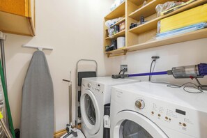A laundry room with two front-loading washing machines, a drying rack, and shelves above containing various laundry supplies. - Hot Tub & Mtn Views! Big Bear All-seasons Escape (Big Bear City)