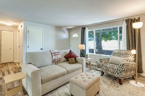 Sala de estar com sofá, pufe, poltrona estampada e mesa lateral com luminária.