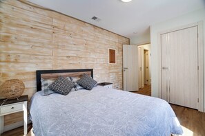 A bedroom with a wooden slat wall, a bed with patterned bedding, a bedside table with a lamp, and a wardrobe. - Walk to Shops & Dining! Poconos Family Getaway (Tannersville)