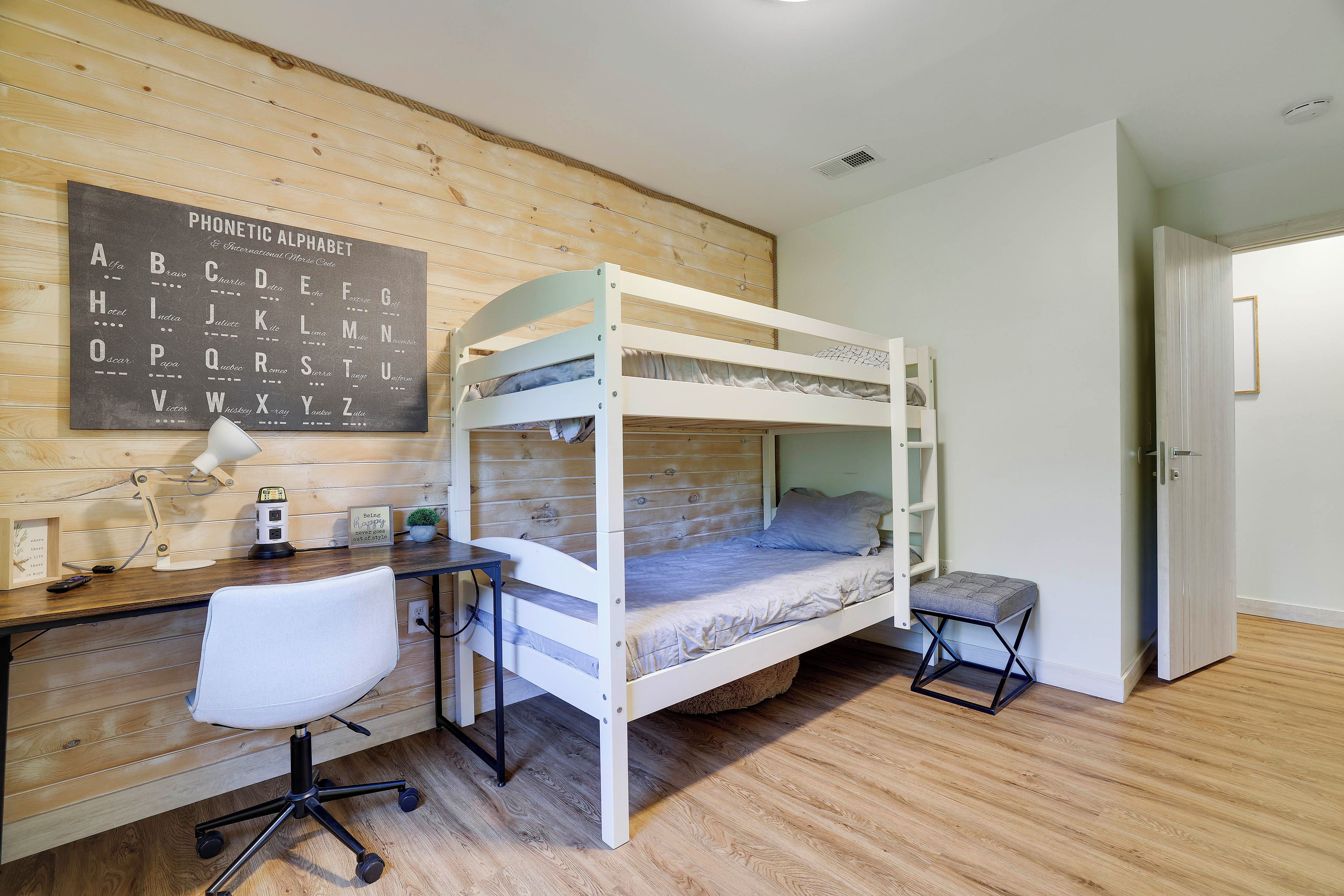 Un lit superposé avec un bureau et une chaise, une affiche de l’alphabet accrochée au mur et une petite plante en pot.