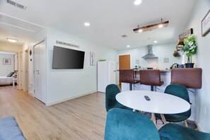 A modern kitchen with a flat-screen TV, a dining area with a round table and chairs, and a living room with a bed and a door leading to another room. - Walk to Shops & Dining! Poconos Family Getaway (Tannersville)