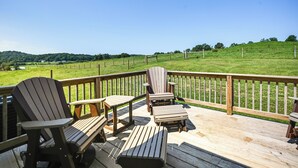 A wooden deck with Adirondack chairs and a table, overlooking a grassy field and a hill. - The Minnie House: Farm Retreat Near Cambridge (Pleasant City)