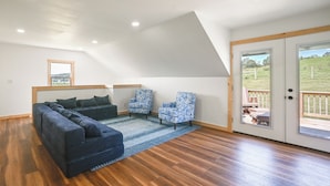 A loft-style bedroom with a sloped ceiling, a large bed, two patterned armchairs, and a view through a glass door to an outdoor deck. - The Minnie House: Farm Retreat Near Cambridge (Pleasant City)
