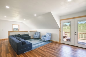 Un dormitorio estilo loft con techo inclinado, una cama grande, dos sillones estampados y vistas a una terraza exterior a través de un ventanal.