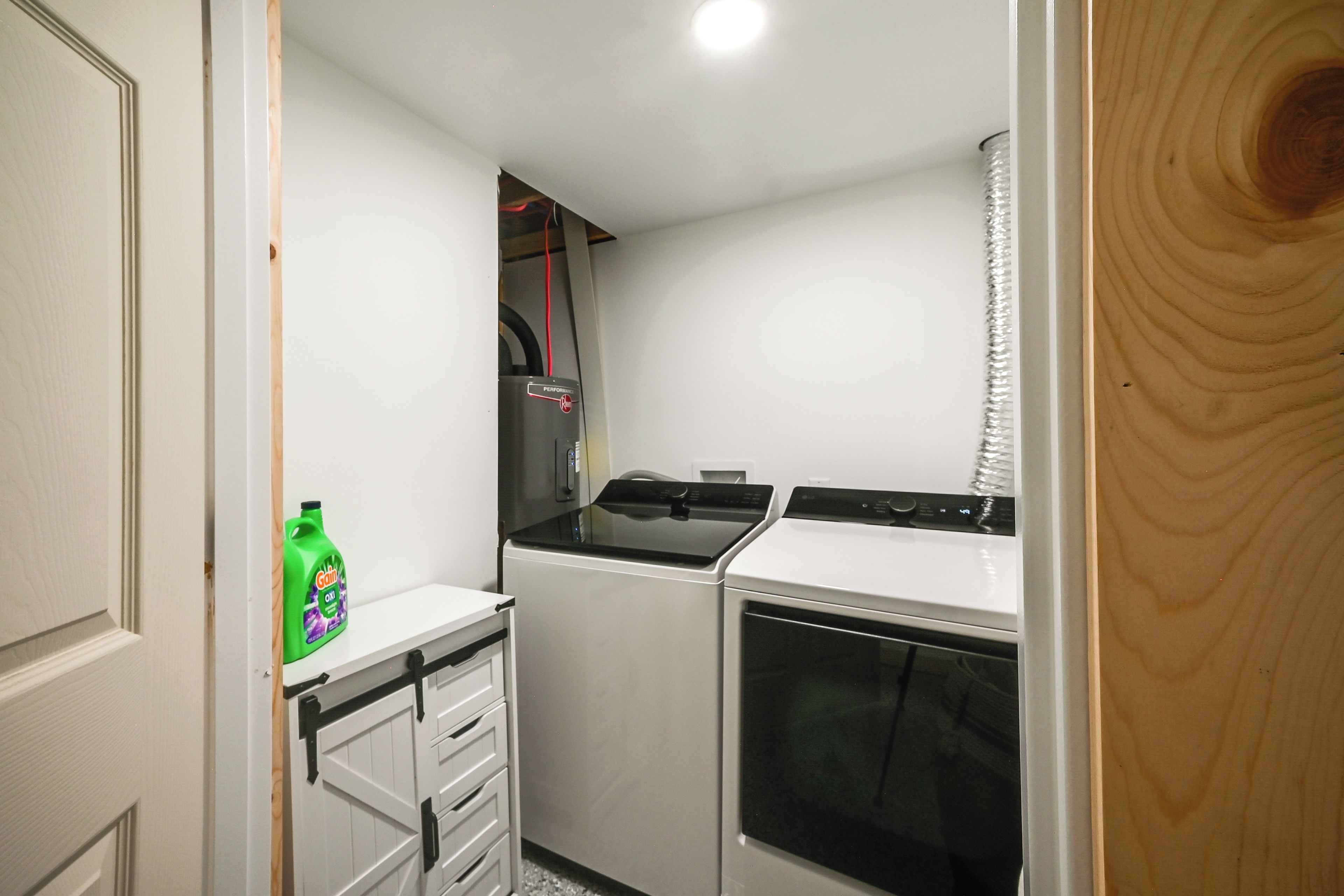 A compact kitchen with a washing machine, a dryer, and a small cabinet with a bottle.