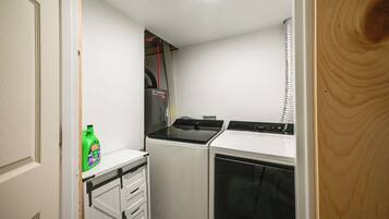 A compact kitchen with a washing machine, a dryer, and a small cabinet with a bottle.
