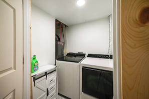 A compact kitchen with a washing machine, a dryer, and a small cabinet with a bottle.