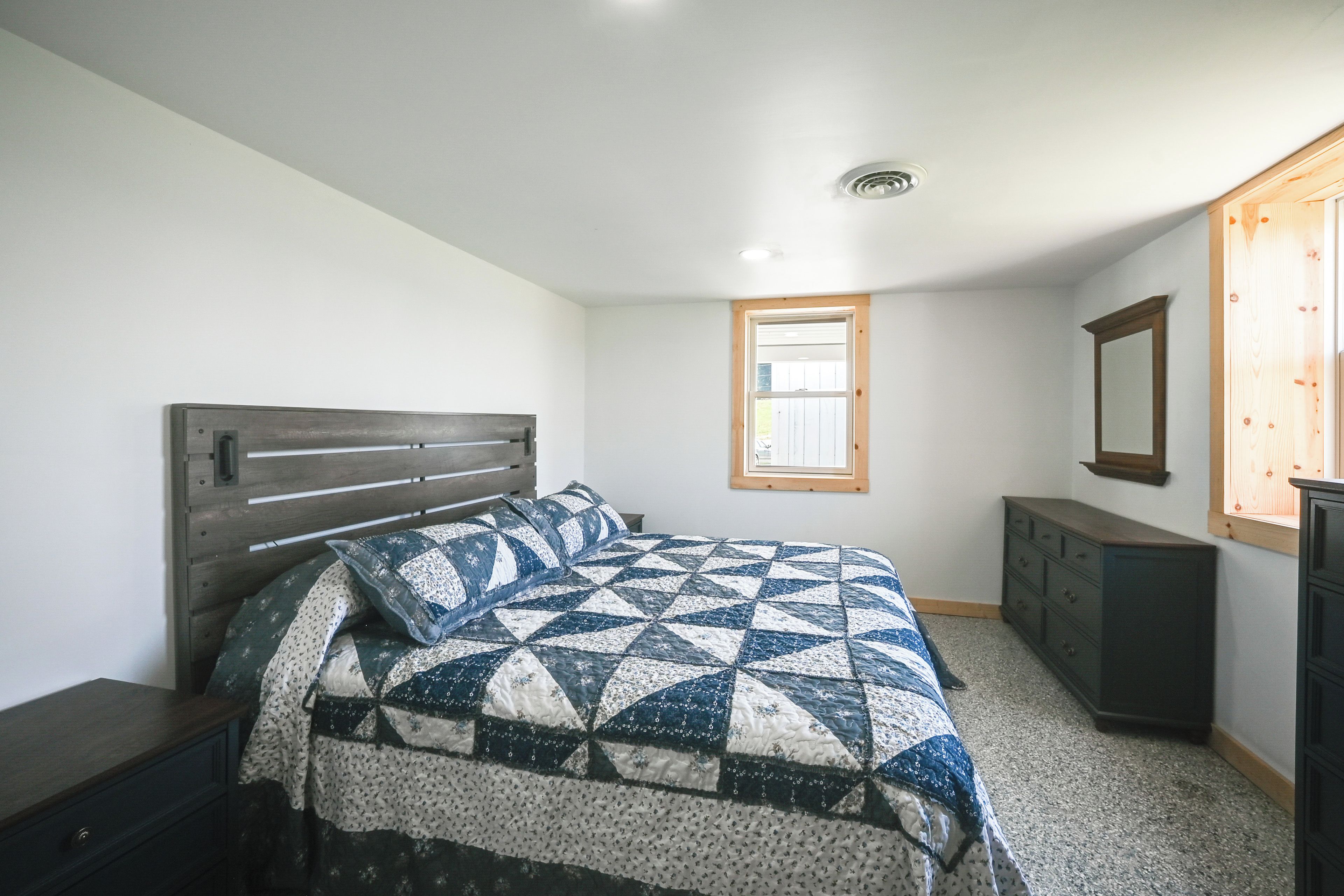 Une chambre à coucher avec un lit, une commode, une fenêtre et un miroir.