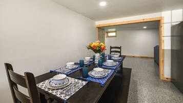 A dining area with a long table set for a meal, chairs, a vase with flowers, and a small window in the background.