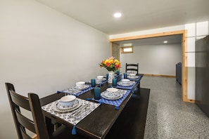 A dining area with a long table set for a meal, chairs, a vase with flowers, and a small window in the background.