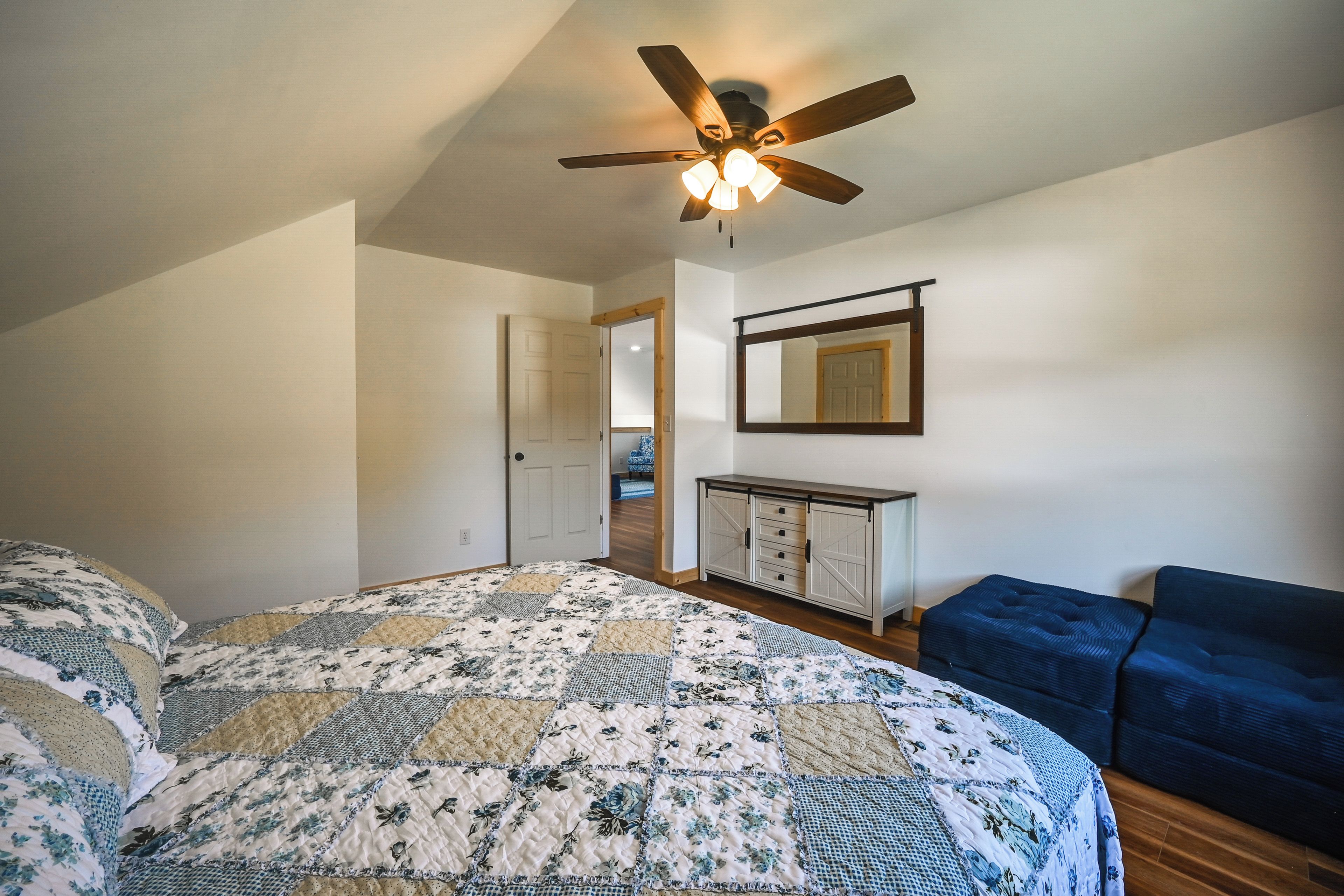 A bedroom with a bed, a ceiling fan, a dresser, and a blue chair.