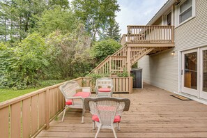 A wooden deck with wicker furniture and a wooden staircase leading to a decked area.