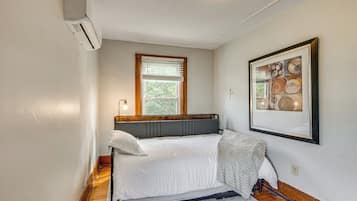 Ein Schlafzimmer mit einem Bett, einem Fenster mit Jalousien, einer Wand-Klimaanlage und einem gerahmten Bild.