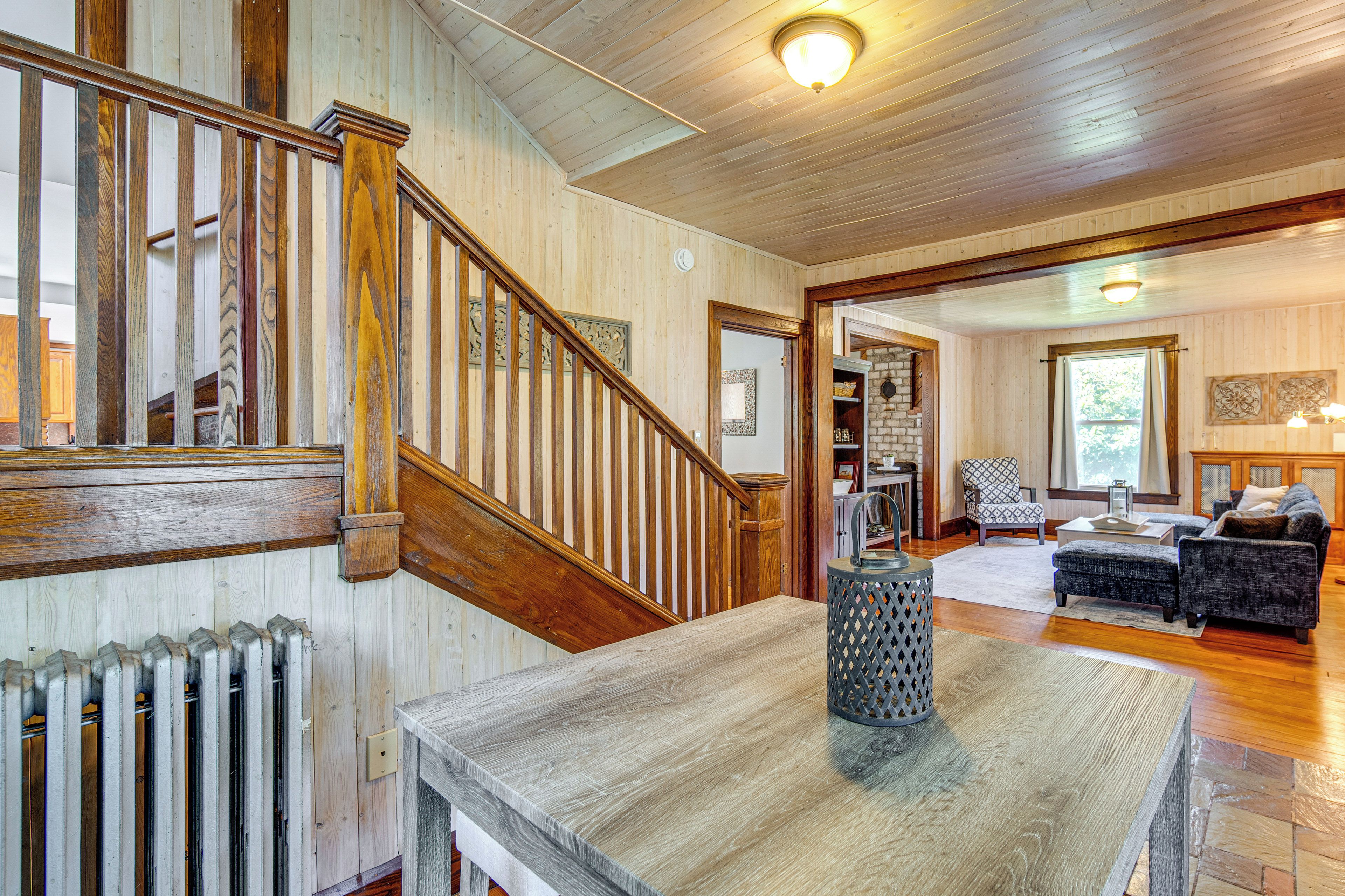 Un escalier en bois mène à un espace de vie comprenant une cheminée, une table à manger et une vue sur l’extérieur.