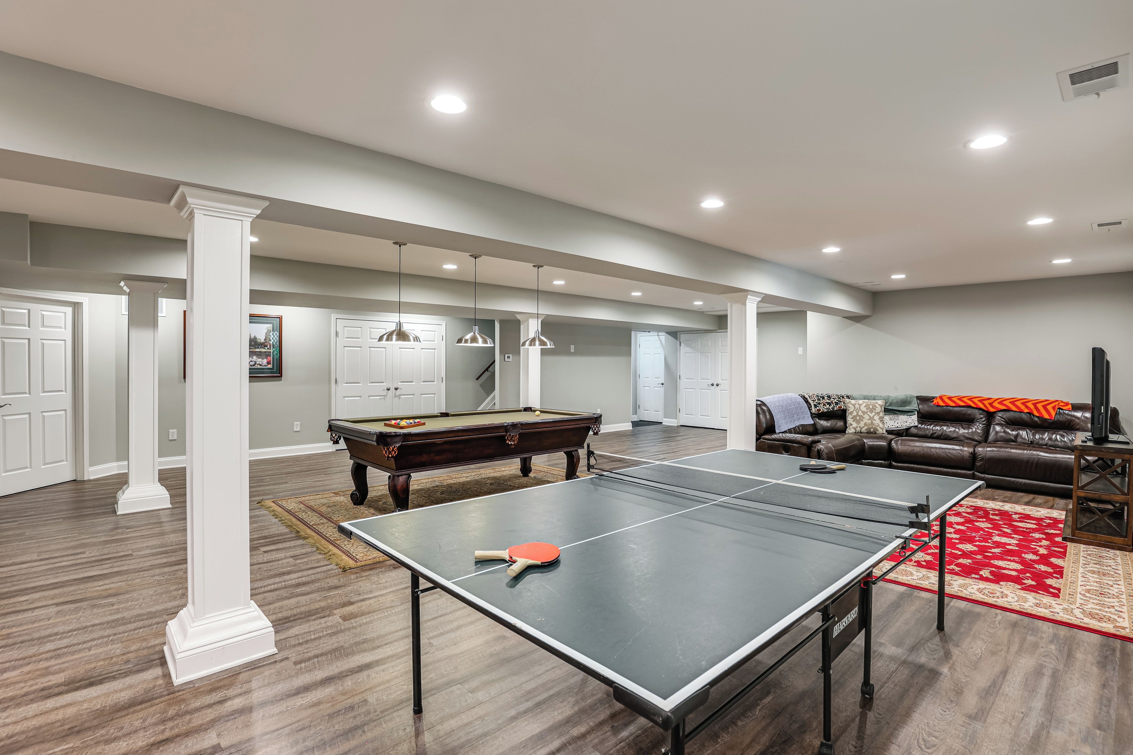 A spacious living area with a pool table, ping pong table, and a leather couch.