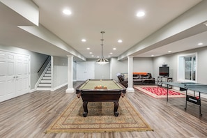 A spacious living area with a pool table, a leather sofa, and a television.
