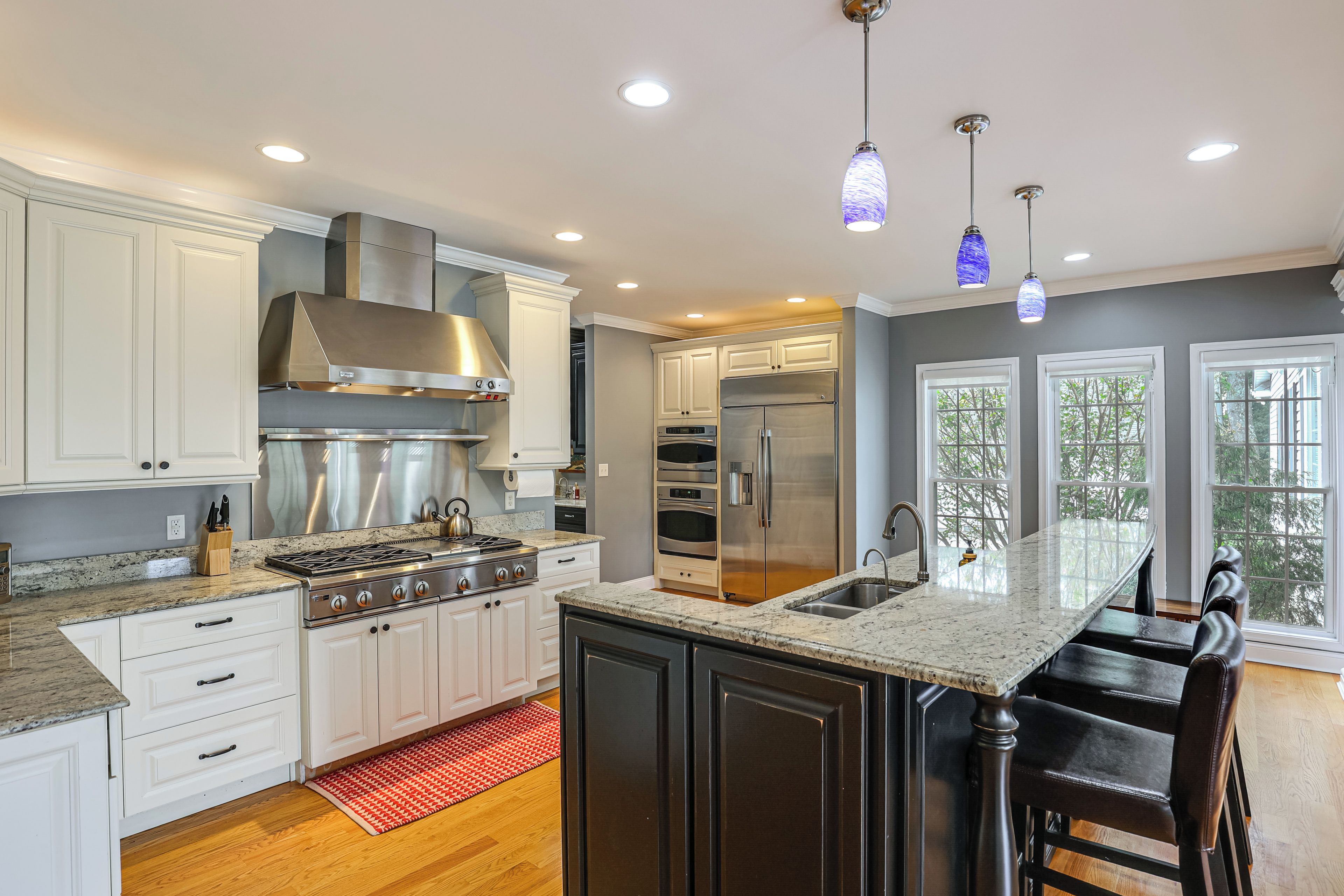 A modern kitchen with white cabinetry, stainless steel appliances, a central island with bar stools, and pendant lighting.