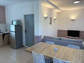 A modern living space with a dining area, a sofa, a TV, and a kitchen area with a refrigerator. - 1-Bedroom Apartment in the Heart of the Combrailles (Pionsat)