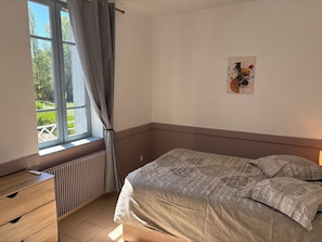 A bedroom with a bed, a radiator, a window with curtains, and a wall with a piece of art. - 1-Bedroom Apartment in the Heart of the Combrailles (Pionsat)