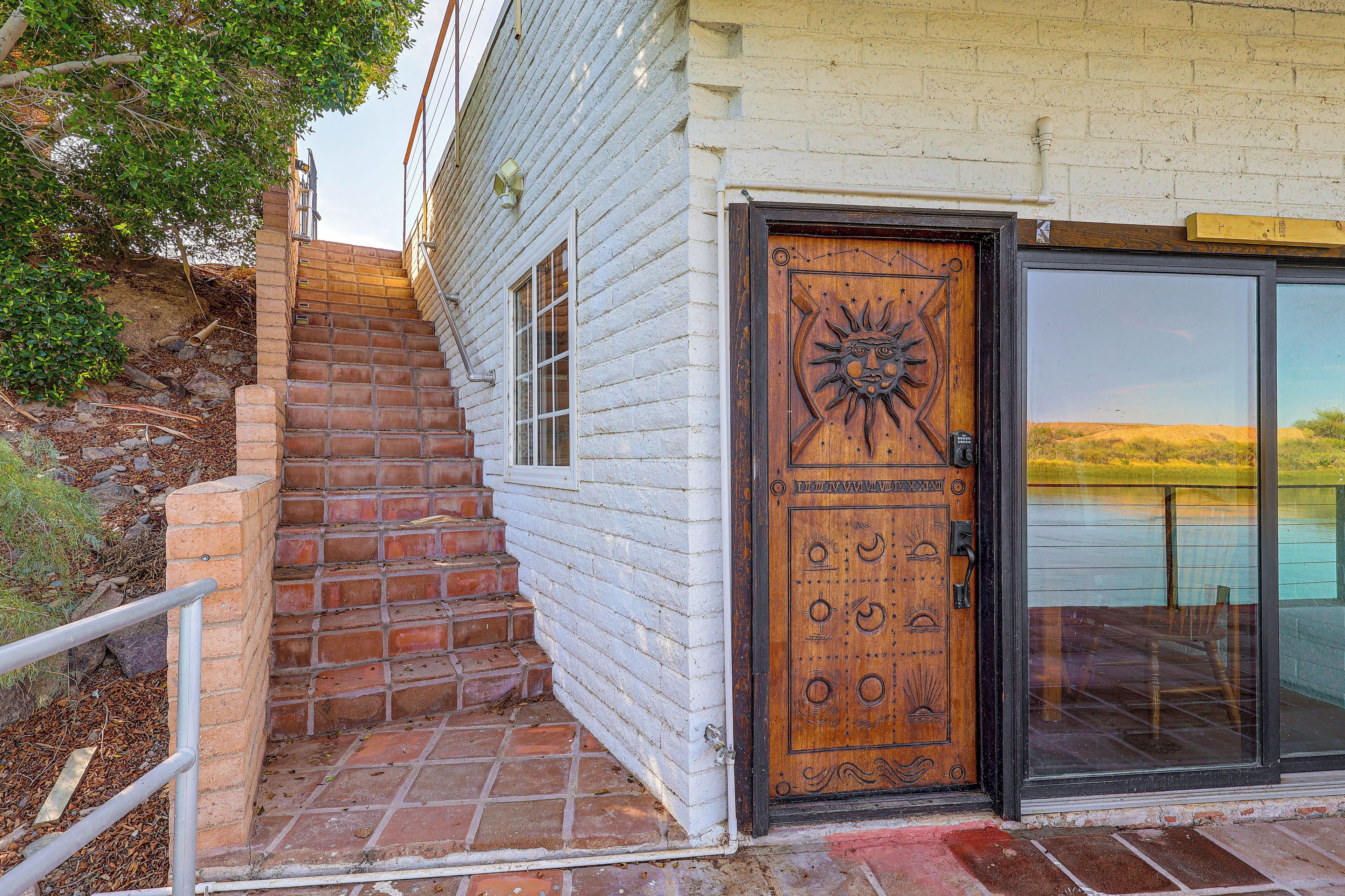 A wooden door with a sun design, a brick staircase, and a glass door leading to a view.