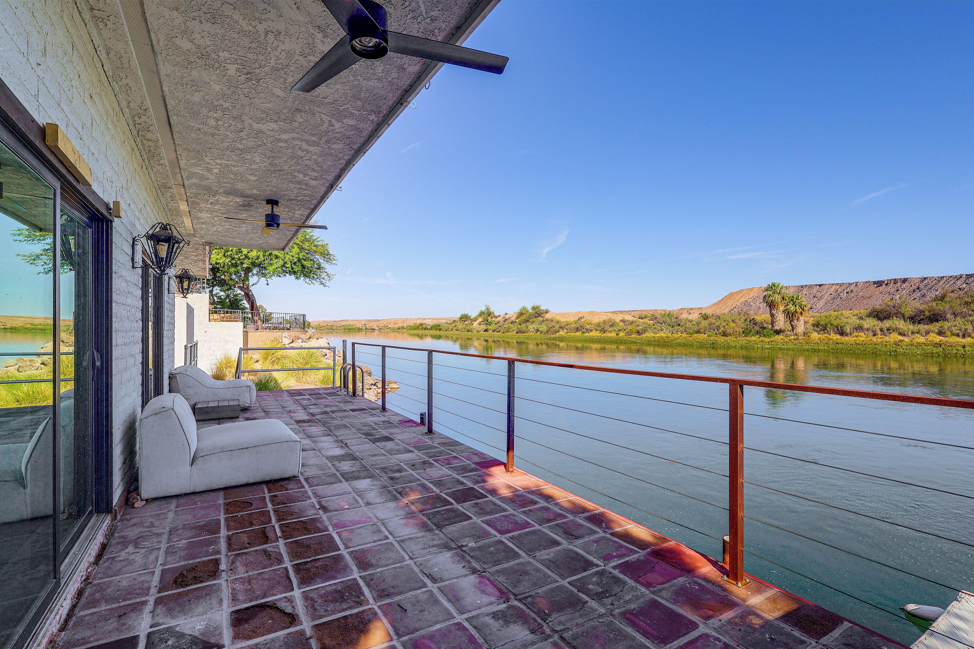 A balcony with a view of a river, a white sofa, and a ceiling fan.