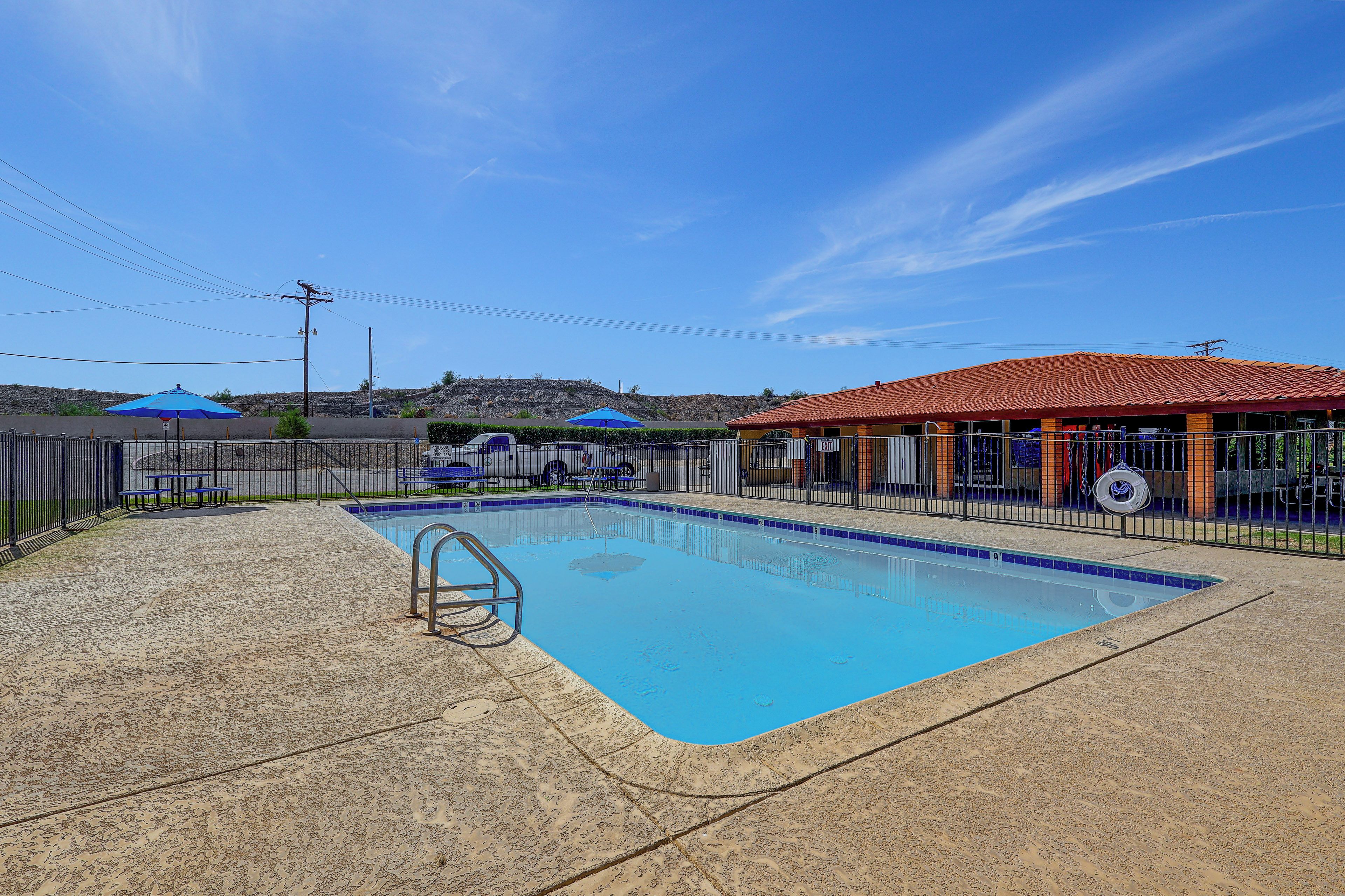 A swimming pool with a metal ladder, surrounded by a fence, and a building with an orange roof in the background.