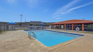 A swimming pool with a metal ladder, surrounded by a fence, and a building with an orange roof in the background.