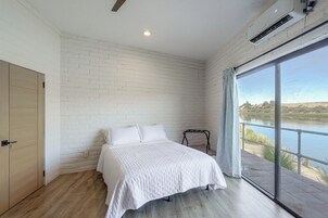 A bedroom with a large window, a bed, and a wooden floor.