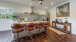Una cocina moderna con una isla central, taburetes de bar, un ventilador de techo y un ventanal grande.