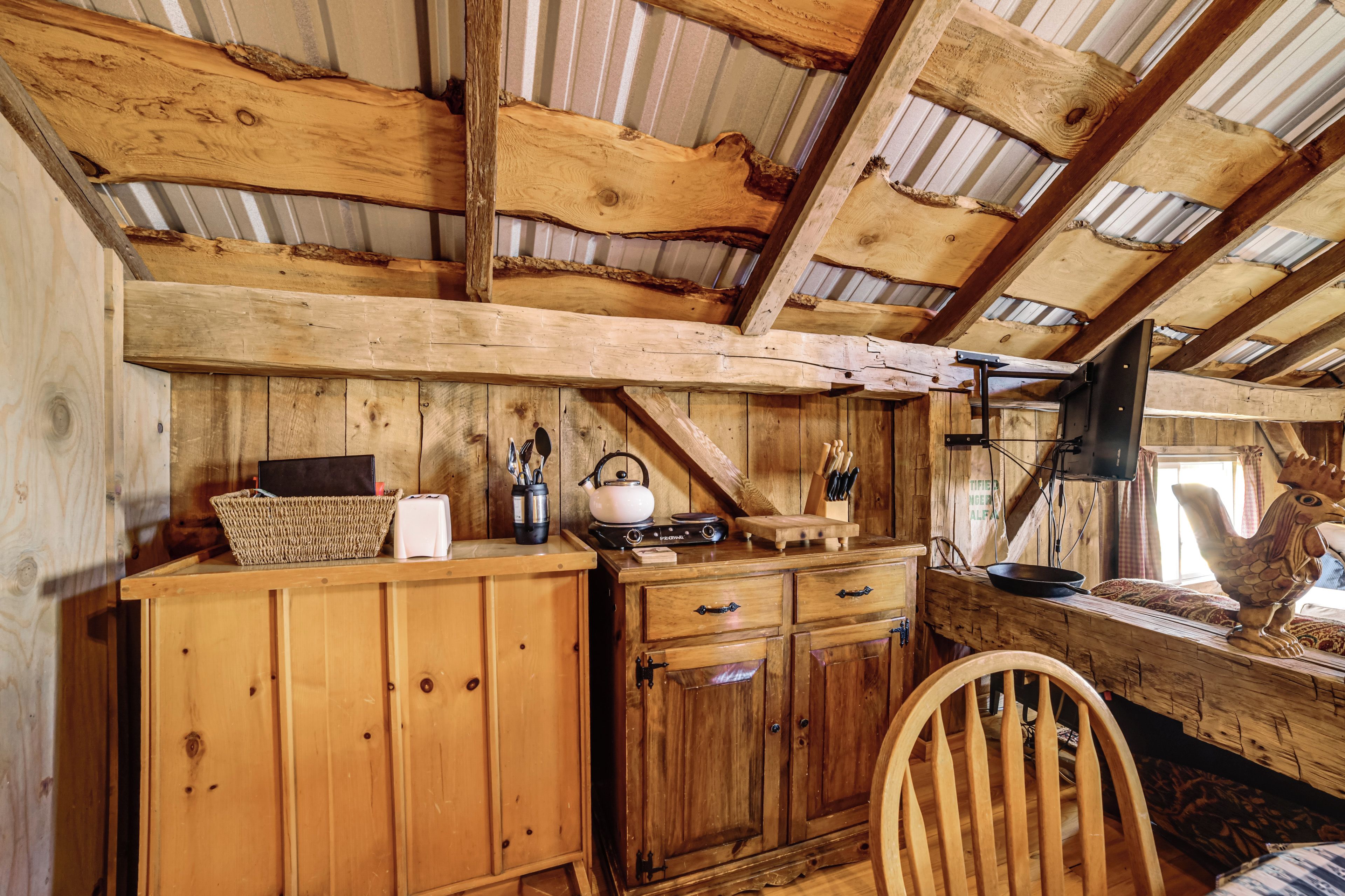 A rustic wooden interior with a high ceiling, wooden beams, a kitchen area with a kettle, and a wooden chair.
