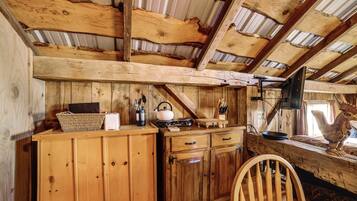 A rustic wooden interior with a high ceiling, wooden beams, a kitchen area with a kettle, and a wooden chair.