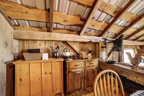A rustic wooden interior with a high ceiling, wooden beams, a kitchen area with a kettle, and a wooden chair.