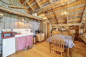 A rustic kitchen with wooden beams, a sink, a microwave, and a dining area with a table and chairs. - On-site Pond: Scenic Farm Stay in Chenango County (De Ruyter)