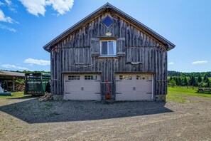 A rustic barn with a gabled roof, two garage doors, and a small window. - On-site Pond: Scenic Farm Stay in Chenango County (De Ruyter)