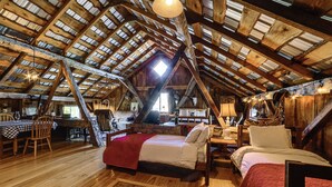 Ein rustikales Schlafzimmer im Dachgeschoss mit schrägen Wänden, Holzbalken, einem Bett, einem Sessel und einem Tisch.
