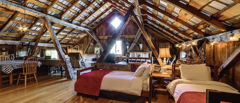 A rustic attic bedroom with a sloped ceiling, wooden beams, a bed, a chair, and a table.