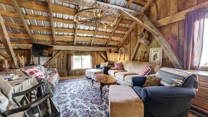 Ein rustikales Interieur mit hoher Holzbalkendecke, einer Kristallleuchter, einem Kamin und einer gemütlichen Sitzecke mit einem gemusterten Teppich.