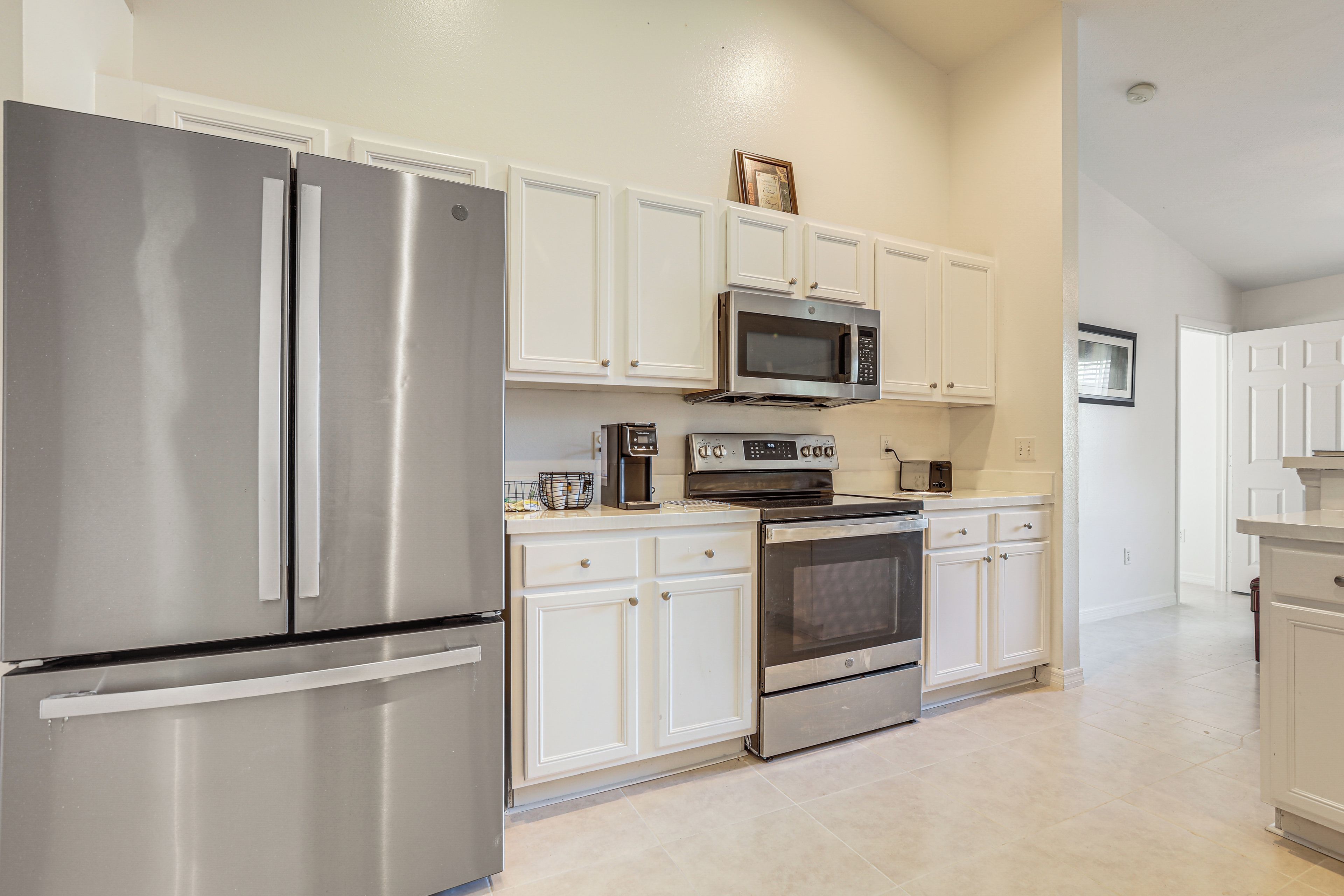 Una cocina con electrodomésticos de acero inoxidable, armarios blancos y piso de baldosas.