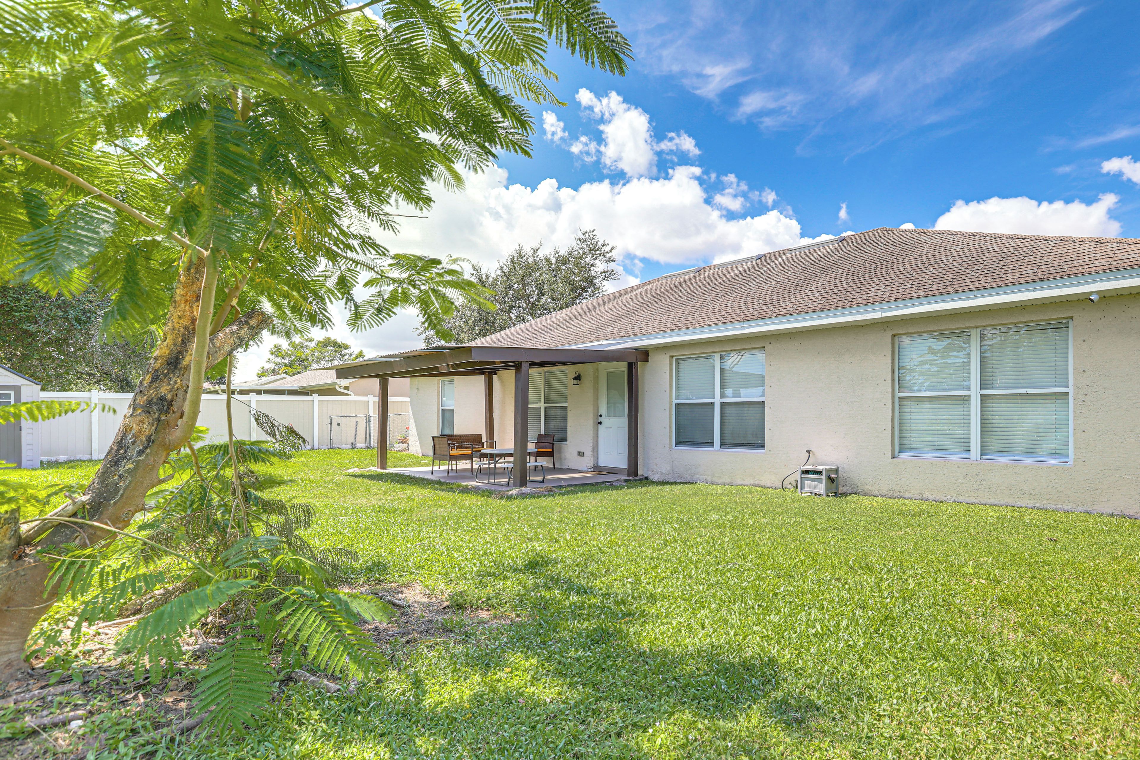 A single-story house with a covered patio, a lawn, and a tree.