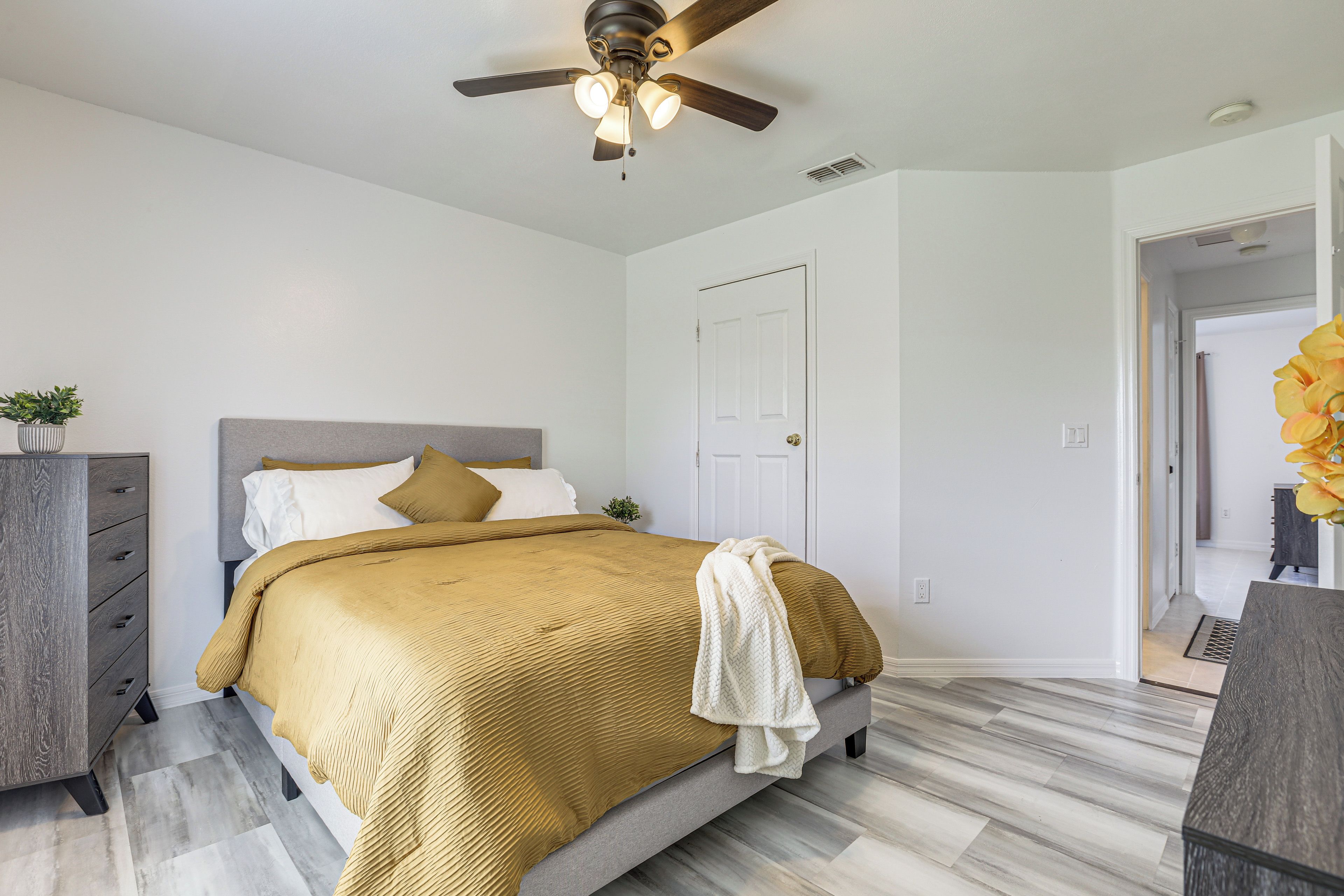 Une chambre à coucher avec un lit, une commode, un ventilateur de plafond et une porte.