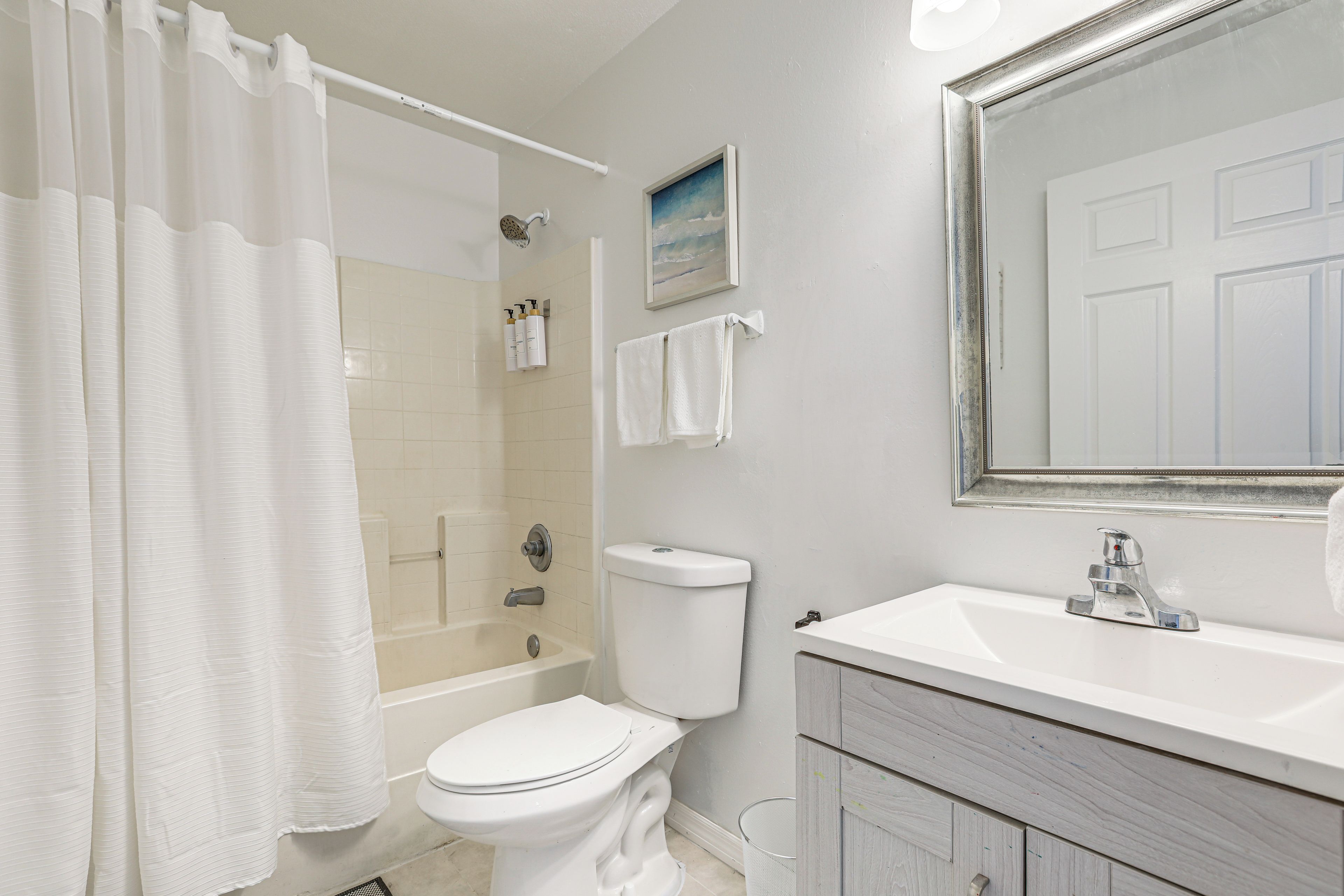 A bathroom with a shower, toilet, sink, and a mirror.