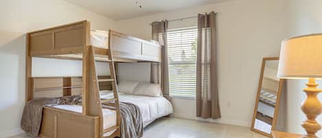 Une chambre avec un lit superposé, un ventilateur de plafond, une fenêtre avec des stores et une table de chevet avec une lampe.