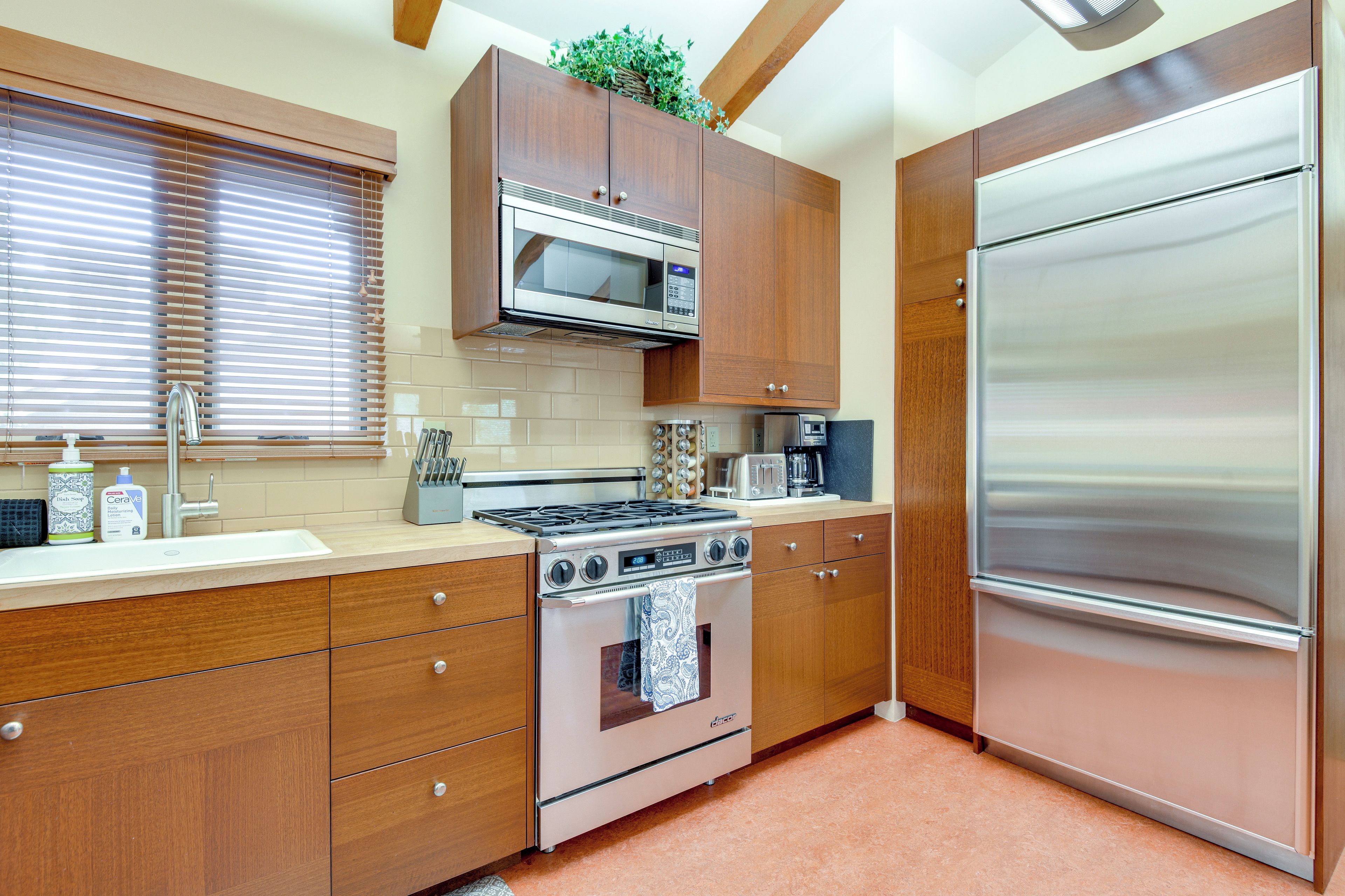 A kitchen with wooden cabinets, a stainless steel refrigerator, a microwave, a stove, and a sink.