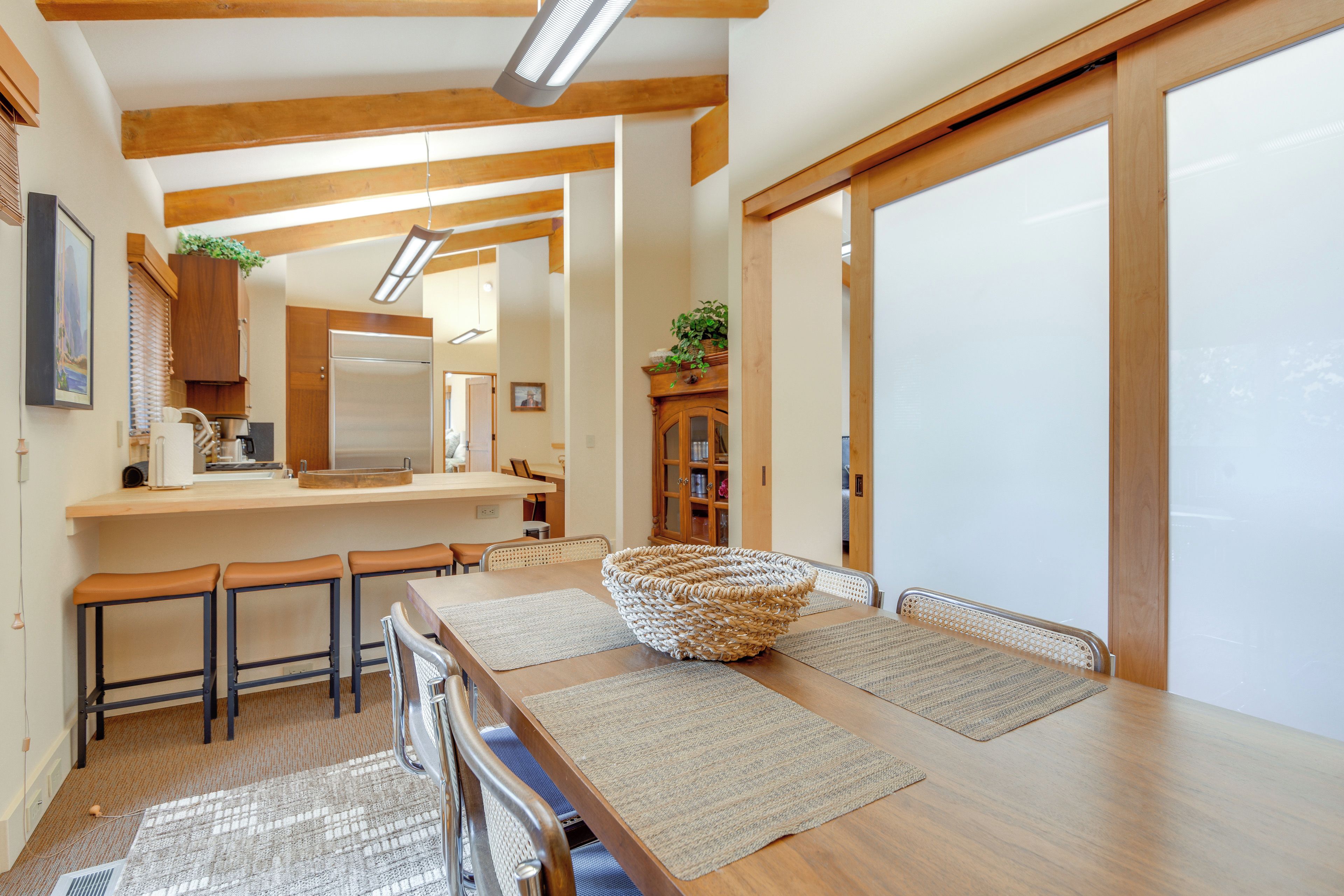 A modern kitchen with wooden beams, a stainless steel refrigerator, and a dining area with a woven basket centerpiece.
