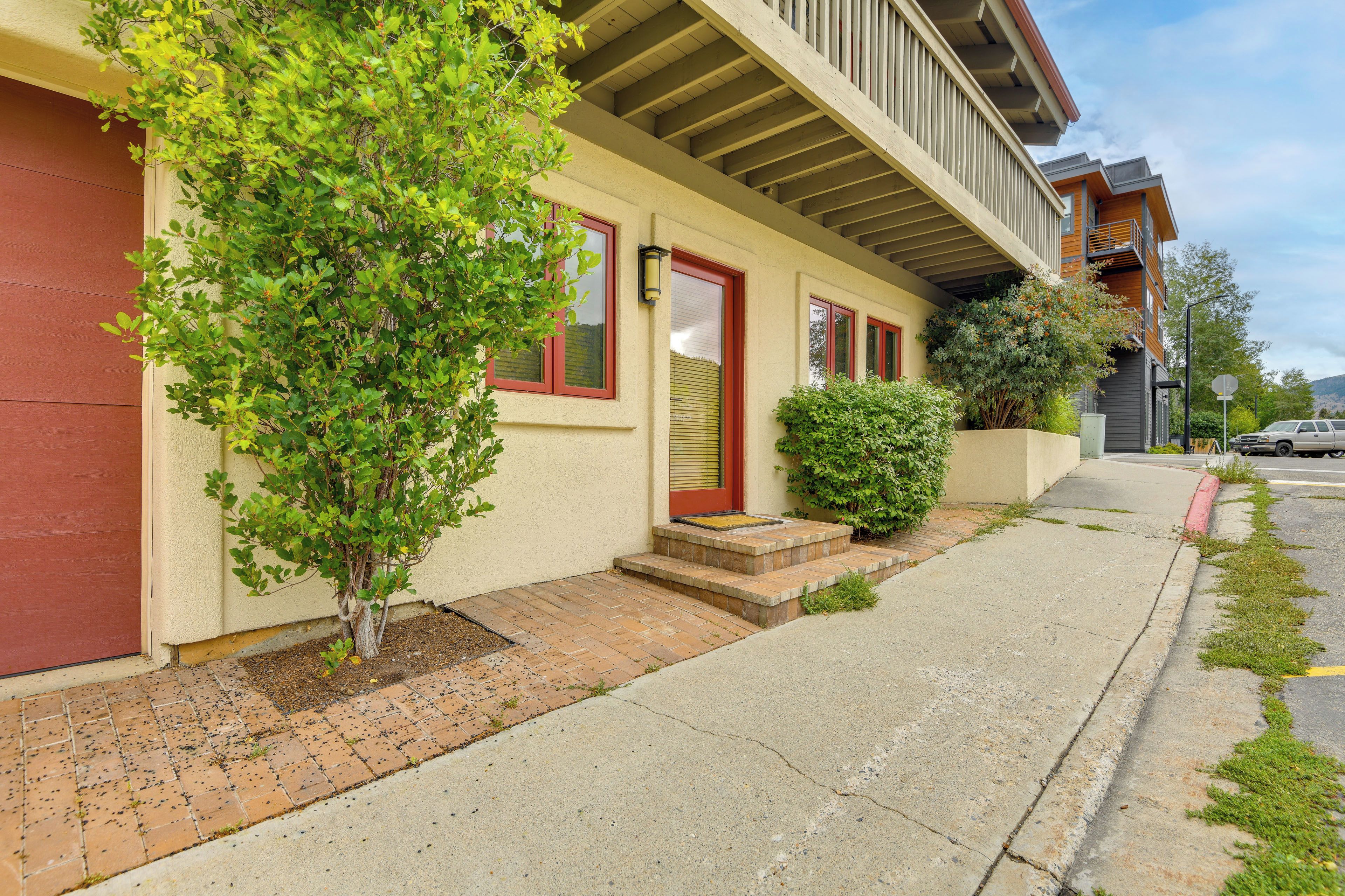 A residential building with a red door, a small front yard, and a vehicle parked on the street.