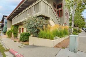 A two-story house with a front porch, a small garden with various plants, and a street view.