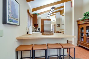 A kitchen with a central island, bar stools, wooden cabinets, and a hanging light fixture.